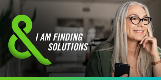 Image of a woman sitting at a laptop and holding a mobile phone with text that says – I AM FINDING SOLUTIONS