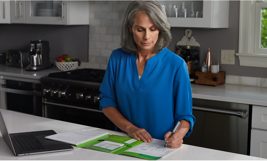 Image of a woman in a kitchen writing on papers on the counter